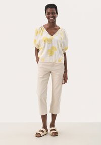 Hvid linned top med gul blomstermønster, V-udskæring og puffærmer, parret med beige cropped bukser og lyse sandaler.