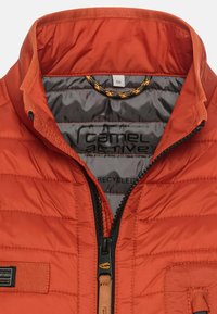 Jacke aus recyceltem Stoff in leuchtendem Orange mit durchgehendem Reißverschluss, genähten Einsätzen und weicher grauer Innenausstattung. Mit Logo und Zubehörschlaufe.