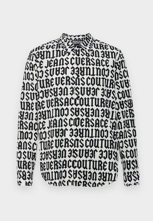 Pitkähihaisen paidan, jossa on mustavalkoinen graafinen kuvio ja toistuva teksti "VERSACE JEANS COUTURE" paksulla fontilla. Napitettava kaulus.