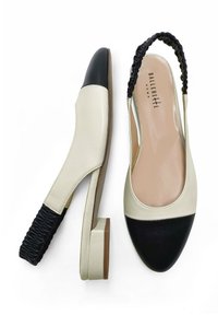 Zapatos de piel beige y negra tipo slingback con puntera redonda, tacón cuadrado y detalle de tirante negro fruncido en la parte trasera. Textura suave.