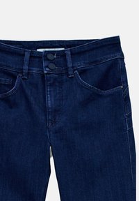 Jeans en denim bleu foncé avec fermeture à double bouton, poches avant, passants de ceinture et détails de couture visibles.