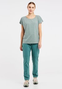 Groene gemêleerde shirt met korte mouwen, gecombineerd met teal lichtgewicht broeken. Sportieve schoenen hebben een gelaagd ontwerp en neutrale kleuren met patroonaccenten.