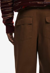 Brązowe spodnie szerokie w nogawkach z teksturowanej tkaniny, z dwoma tylnymi kieszeniami i wysokim stanem. Akcentowane ciemnoczerwonym swetrem knit.