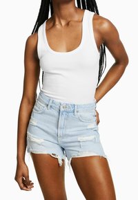 Vit ribbad linne tillsammans med ljusblå slitna denimshorts med fransad nederkant och synliga fickor.