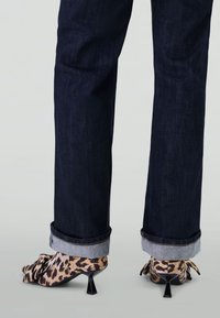 Dark rolled-up jeans paired with leopard print heeled shoes featuring large bows on the front, shown from the back.
