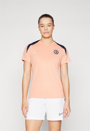 Tricou sportiv piersiciu cu accente bleumarin, guler rotund și mâneci scurte. Prezintă logo-ul Chelsea FC și swoosh-ul Nike în aur pe piept.