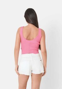 Roosa ribidega tank top, millel on ümmargune seljatagune, koos valgete rebenditega denimpükstega. Kangas on kehas tekstuuriga viimistlusega.