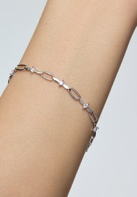 Srebrna bransoletka z wydłużonymi ogniwami na przemian z małymi okrągłymi kamieniami szlachetnymi, prezentowana na skórzanej ręce w odcieniu skóry.