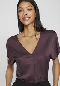 Bordo trumpa rankovė bluzonė, pagaminta iš satino; turi giliu V formos iškirpimu ir minimaliai siūlių detalių. Lygus paviršius su laisvu siluetu.