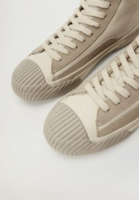 High-top tenisky z béžové kůže s texturovanou suedovou boční částí. Mají gumovou špičku s vroubkovaným detailem a ploché tkaničky.