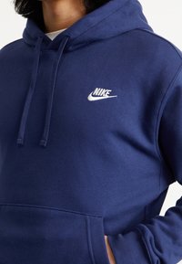 Felpa con cappuccio Nike blu navy con tasca frontale, cappuccio con coulisse e logo ricamato. Realizzata in tessuto morbido e dalla texture ruvida con polsini a coste.