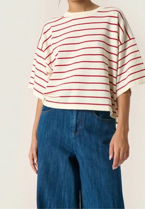 Personne portant un haut blanc ample à rayures horizontales rouges et un jean en denim bleu taille haute à jambes larges, visible du cou aux hanches.