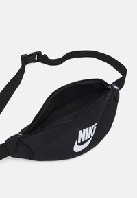 Svart midjeväska i texturerad nylon. Har ett ficka med dragkedja och en justerbar rem. Stor vit Nike-logotyp på framsidan.