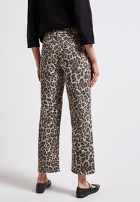 Pantaloni a gamba larga con stampa leopardata in beige e nero, dotati di design a cinque tasche e vita media, abbinati a ballerine nere.