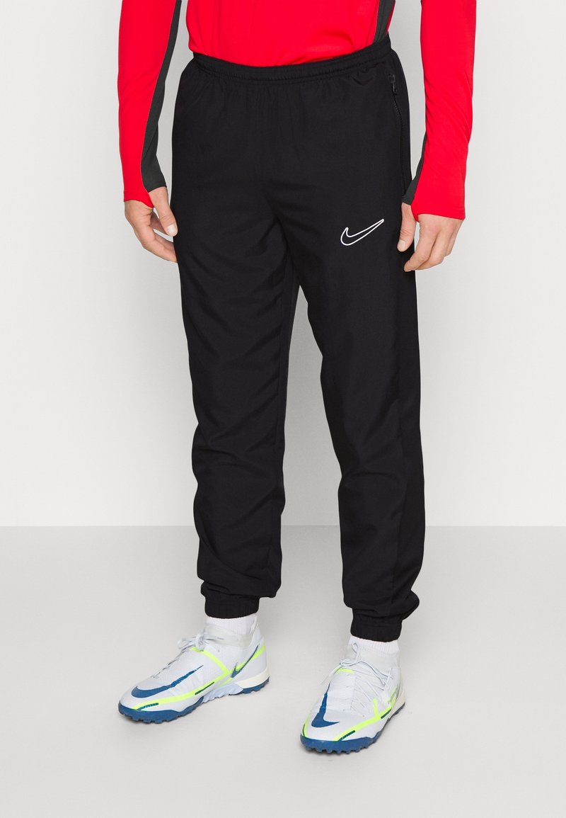 Pantalons de survêtement Nike noirs avec une taille élastique, des jambes fuselées et un détail de logo blanc. Le matériau semble léger et lisse.