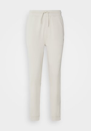 Light beige sweatpants made of soft, textured fabric. Features a drawstring waistband, ribbed cuffs, and side pockets. Tailored fit.