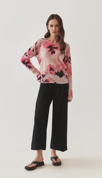 Rosa und schwarzer Pulli mit Blumenmuster aus weichem Material, kombiniert mit schwarzen weit geschnittenen Hosen und schwarzen Flip-Flop-Sandalen.