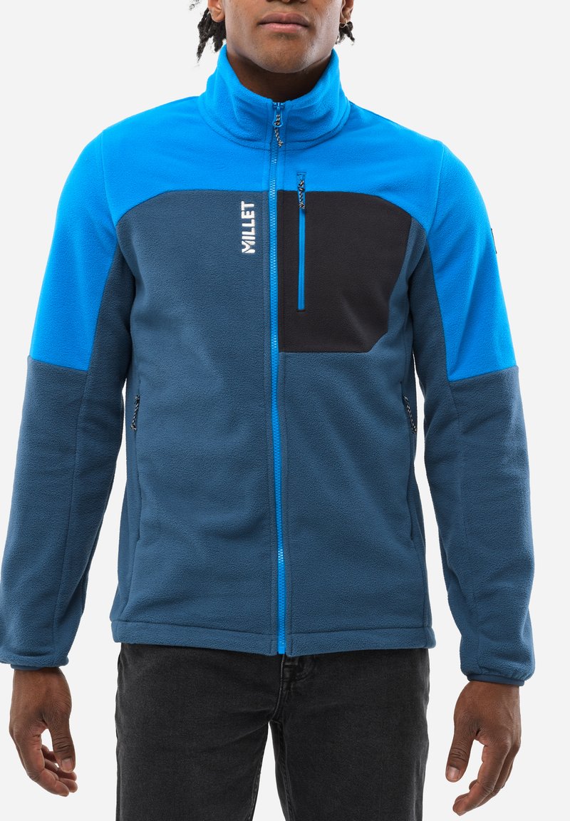 Fleece jacket in blue with black paneling. Features a high collar, zippered chest pocket, and contrasting zippers. Soft texture.