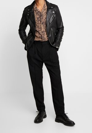 Zwarte leren motorjack over een bruine panterprint blouse, gecombineerd met zwarte geplooide broek en zwarte veterschoenen.