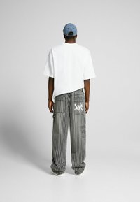 T-shirt bianco oversize, pantaloni cargo grigi a righe con tasche laterali e dettagli grafici bianchi, abbinati a un cappellino di denim blu.