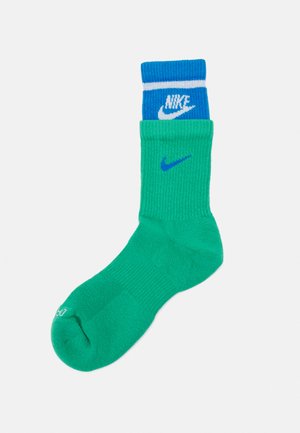 Meia de algodão verde com punho canelado azul. Apresenta a marca branca da Nike no punho e um logótipo azul menor na lateral.