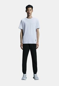 White short-sleeve t-shirt, black pants, gray shoes with accents, presented on a model against a plain background. Simple design and fit.