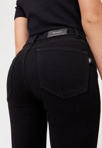 Zwarte denim jeans met een slim fit, voorzien van twee achterzakken en een merketiket op de tailleband. De stof heeft een gladde textuur.