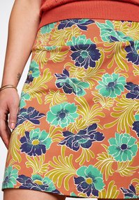 Spódnica w kwiatowy wzór z koralowym tłem oraz dużymi turkusowymi i granatowymi kwiatami. Materiał ma gładką teksturę i dopasowany krój.