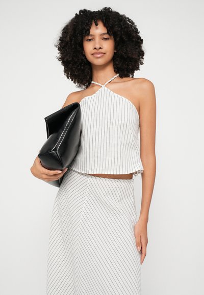 Top sin mangas blanco con rayas verticales negras, con dobladillo deshilachado; combinado con una falda de patrón similar. La modelo sostiene un bolso de mano negro.