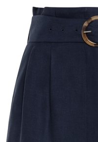 Jupe bleu marine en tissu texturé, avec une large ceinture à passants et une boucle de ceinture ronde marron.