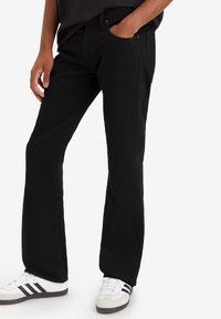 Jeans negros acampanados con detalles sutiles de costura, bolsillos delanteros y cintura de tiro medio, combinados con zapatillas blancas con acentos negros.