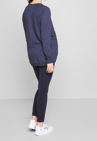 Felpa a maniche lunghe blu navy con polsini e orlo a coste, abbinata a leggings blu navy e scarpe da ginnastica bianche con strisce colorate.