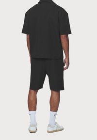 Czarna koszulka z krótkim rękawem i dopasowane szorty wykonane z fakturowanego materiału. Noszone z białymi skarpetami i jasnymi sneakersami.