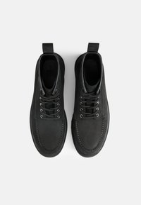 Zapatos de cuero negro con una textura suave, puntera redondeada, seis ojales y costuras en contraste, con una lengüeta en el talón.