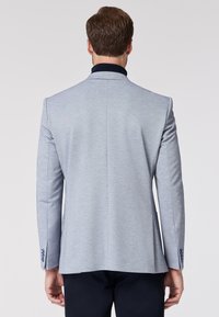 Blazer grigio chiaro con finitura testurizzata, colletto blu, vestibilità su misura, spacco posteriore singolo e bottoni decorativi blu sui polsini.