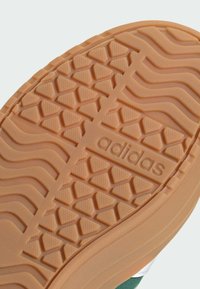 Semelle de chaussure Adidas avec un design en caoutchouc orange texturé, présentant un motif triangulaire, un logo en relief et des détails de bord lisses.