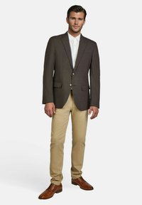 Donkerbruine blazer met twee knopen, een zak en een geknipt revers, gedragen met lichtbruine broeken en bruine leren schoenen.