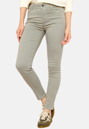 Slim-fit light gray pants worn by a person standing with one leg slightly crossed over the other, paired with beige and olive sneakers.