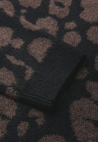 Tessuto a maglia con un motivo a stampa leopardo marrone e nero. Dettaglio del polsino nero a coste. Superficie strutturata, aspetto caldo e morbido.