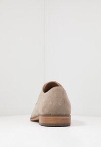 Beige Wildleder-Schuh mit abgerundetem Zeh und niedrigem Holzabsatz. Verfügt über eine gestickte Verzierung auf der Rückseite und ein glattes Innenfutter.