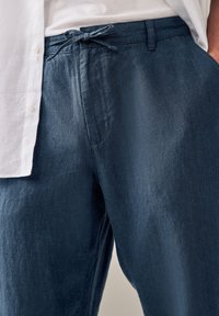 Pantaloni in lino blu con vestibilità rilassata, dotati di chiusura con cordoncino, tasche laterali e una finitura leggermente testurizzata.