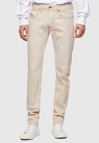 Jeans de mezclilla en un tono beige claro con corte ajustado, que presentan una textura desgastada y un clásico diseño de cinco bolsillos. Combinados con zapatillas blancas.
