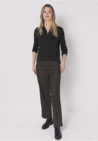 Zwart lang mouw zip shirt gecombineerd met bruine geruite broek en zwarte enkellaarsjes. Soepele stoftextuur met een getailleerde pasvorm.