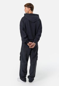 Φαρδύ σκούρο γκρι φούτερ με μεγάλο καπέλο, συνδυασμένο με ταιριαστά άνετα cargo παντελόνια, που διαθέτουν πλάγιες τσέπες και χαλαρή εφαρμογή.