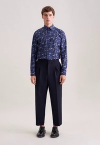 Camicia a maniche lunghe blu navy con motivo floreale, abbinata a pantaloni scuri a vita alta. La camicia presenta un colletto con bottoni e una vestibilità regolare.