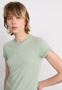 Rövid ujjú, testhez simuló, világoszöld pamut póló, amelyen egy kis ezüst Nike logó látható a mellrészen, illetve kerek nyakú kialakítású.