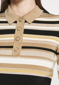 Kragenoberteil mit geripptem Design, das horizontale Streifen in Beige, Schwarz, Weiß und Gelb aufweist, sowie vier runde Metallknöpfe auf der Vorderseite.