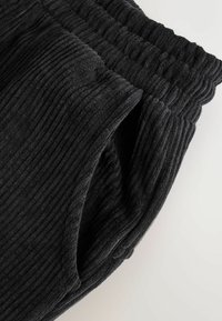 Sorte ribbede stofbukser med elastisk talje, der har en blød tekstur og samlede detaljer øverst for en tætsiddende pasform.