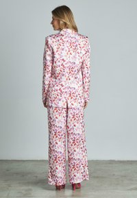 Completo floreale multicolore con blazer aderente e pantaloni a gamba larga, realizzato in tessuto morbido. Presenta motivi di foglie rosa e viola.