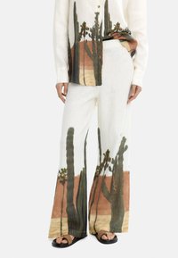 Lnianowe, białe spodnie typu wide-leg z nadrukiem kaktusa na pustyni w odcieniach zieleni i brązu, w komplecie z dopasowaną koszulą zapinaną na guziki.